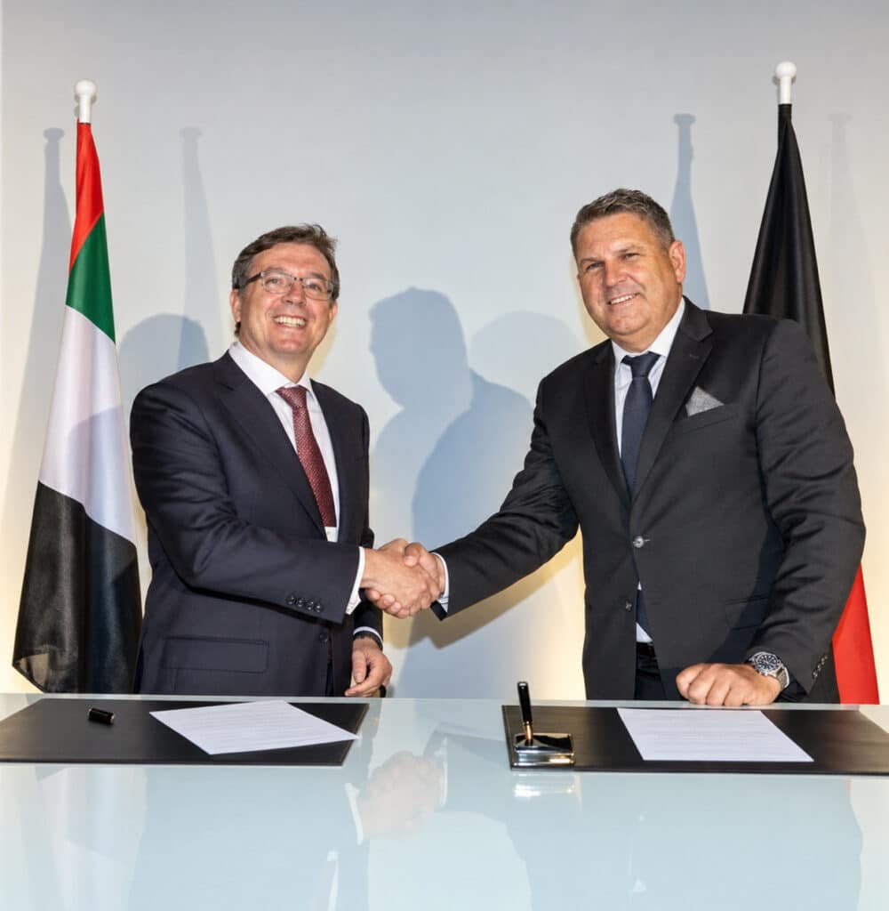 Axel Ebbecke shaking hands with someone in front of the flags of Germany and the United Arab Emirates.
